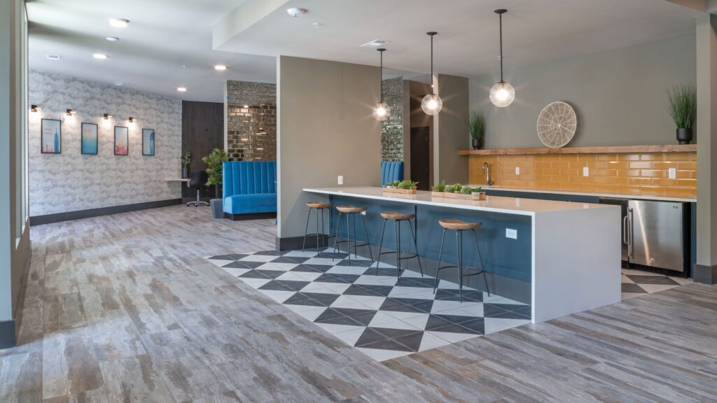 Modern communal area with an island counter and stools, geometric floor tiles, blue booth seating, and wall decor.