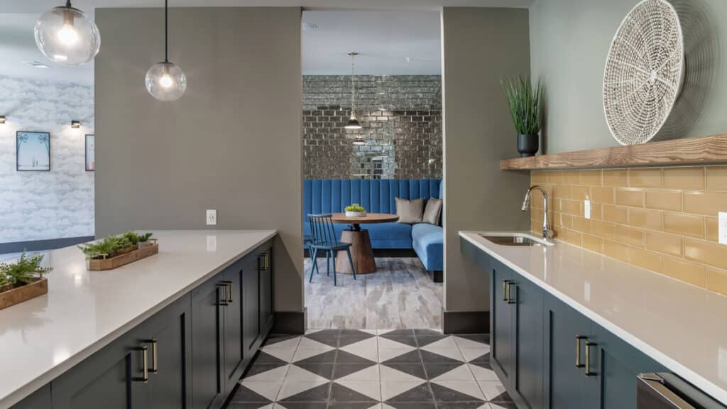 Modern kitchen with dark cabinets, white countertops, and pendant lights, leading to a dining area with blue booth seating and mirrored wall.